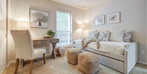 A bedroom with a bed, desk, and chair. The bed is covered with white pillows and a blanket. There is a picture on the wall above the desk. AI generated content